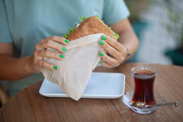 Woman Holding Sandwich. Casual Lunch with Sandwich in Woman&rsquo;s Hand. Quick Meal Concept with Woman Holding Sandwich. Street Food Sandwich Held by Woman. Young Woman Eating Sandwich.