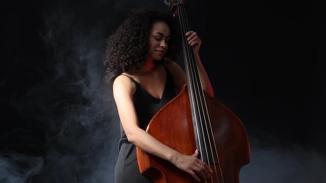 Woman playing double bass on black background with smoke