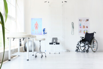Fototapeta premium Blurred view of physiotherapist's office with couch, sports equipment and wheelchair