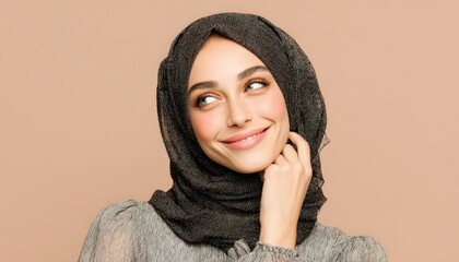 Young woman wearing a dark textured head covering smiles thoughtfully against a neutral background