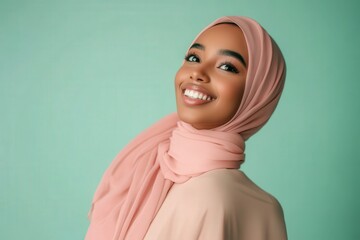 Attractive young woman with dark skin radiates joy wearing a soft pink head covering against a pale green background