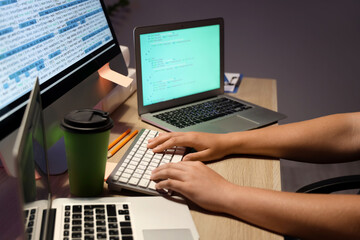 Male programmer working with computer keyboard and modern laptops at table in office, closeup