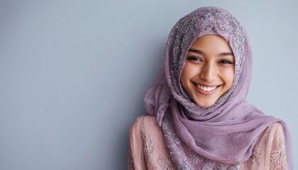 Young woman wearing a decorative head covering smiles brightly against a plain backdrop