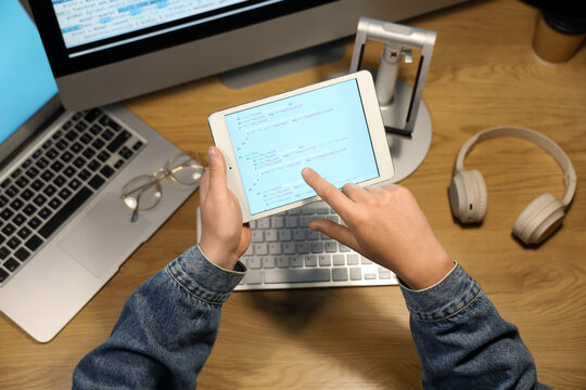Programmer's hands pointing at modern tablet computer on wooden background