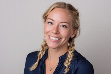 Smiling young adult woman with blonde hair styled in braids poses for a headshot against a neutral background.