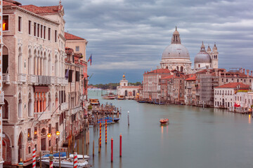 Naklejka premium A view of the Grand Canal in Venice, Italy with boats, historic buildings, and the Basilica di Santa Maria della Salute under a cloudy sky.