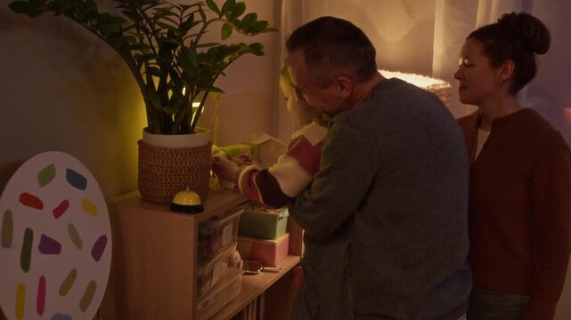 Loving Caucasian family cleaning up kid room together. Father helping little daughter to place plush toy on bookcase