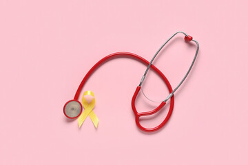 Fototapeta premium Yellow ribbon with stethoscope on pink background. Childhood cancer awareness concept
