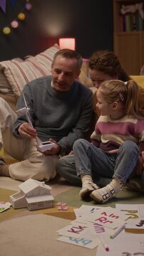 Vertical shot of Caucasian family of three sitting on floor, spending spare time together. Father showing plastic model of windmill