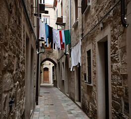 Obraz premium A narrow alley with textured stone walls and laundry lines, muted colors, lived-in atmosphere