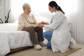 Physical therapist with senior woman holding hands in bedroom