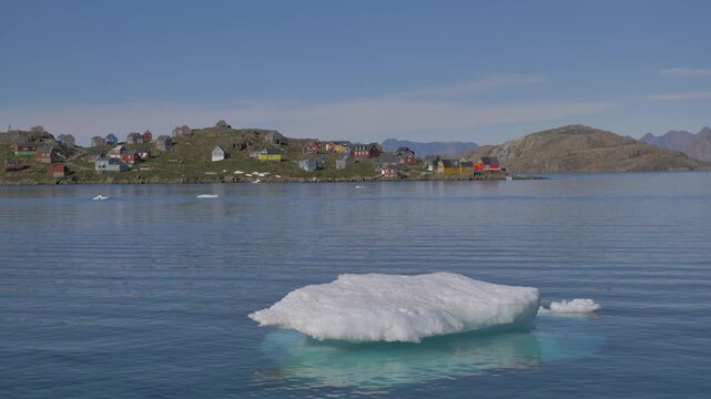 An iceberg floating in the bay of Kulusuk, a small village in Greenland, with its typical colorful Nordic houses in the background. Similar footage available in my portfolio.