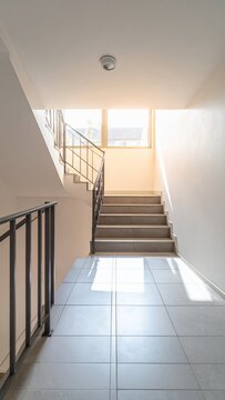 Bright and empty modern staircase with natural light from a window, leading upwards in a clean building interior.