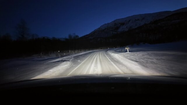 Dashboard camera view from a white sports utility vehicle driving through a winter wonderland at night.