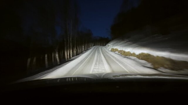Dashboard camera view from a white sports utility vehicle driving through a winter wonderland at night.