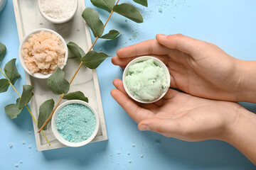 Female hands with scrubs, sea salt and eucalyptus on blue background. Body massage concept © Pixel-Shot