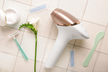 Fototapeta premium Modern photoepilator with wax strips, jar of cream and razor on white tile background