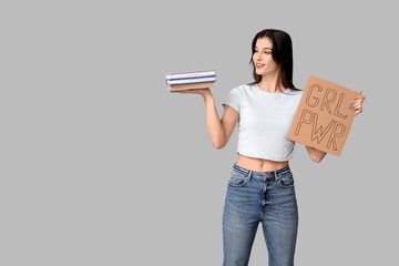 Young woman holding cardboard with text GRL PWR and books on grey background. Feminism concept