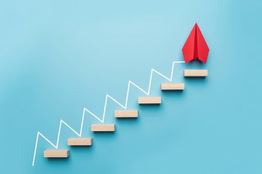 Red paper airplane ascending a stepped path