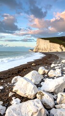 Coastal vista of rocks, beach, and cliffs under a cloudy sky with pink hues at sunset or sunrise, serene seascape