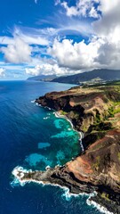 Obraz premium Aerial view of rugged coastline with blue ocean and cloudy sky
