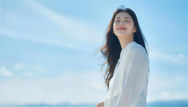 青空を背景に風を感じて目を閉じる笑顔の女性