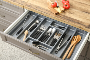 Open kitchen drawer with different silver cutlery and fresh tomatoes on board