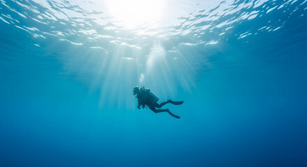 Scuba diver swimming deep underwater with sun rays shining throu