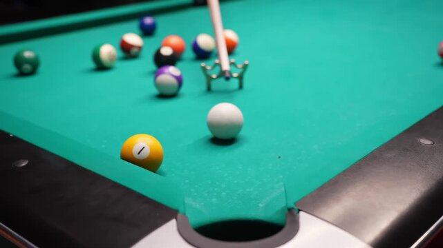 Pool table close-up as a cue aims at the red 3 and it drops into a pocket, with scattered solids and stripes on green felt in a cinematic pub game scene.