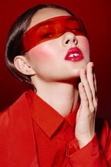 Fashion model in red clothing poses with glossy lips and pink makeup wearing futuristic red translucent visor this beauty creative portrait expresses bold style mood.