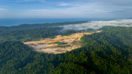 Obraz premium Aerial photo of a terraced limestone quarry on a tropical island landscape, revealing stepped rock formations, quarry roads, and large extraction zones surrounded by dense forest cover.