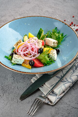 Fresh horiatiki salad featuring creamy feta, Kalamata olives, ripe tomatoes, crisp cucumber, purple onion and mixed lettuce on rustic blue plate. Authentic Greek village salad