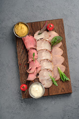 Assorted sliced roast beef and pork on rustic wooden board with mustard and horseradish sauces, cherry tomatoes and fresh greens garnish. Gourmet meat platter, elegant charcuterie-style appetizer