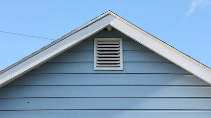 Naklejka premium Blue wooden gable with white ventilation grille under pale sky, horizontal siding and roofline that emphasizes home airflow.