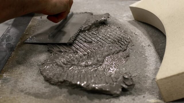 Close-up of mason spreading gray mortar with trowel onto oven base for curved refractory piece.