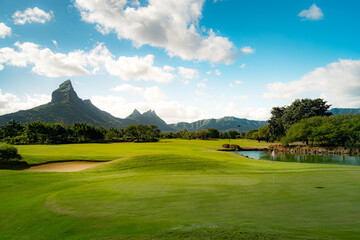 Obraz premium Panoramic Golf Course with Majestic Mountains and Tranquil Lake at Golden Hour