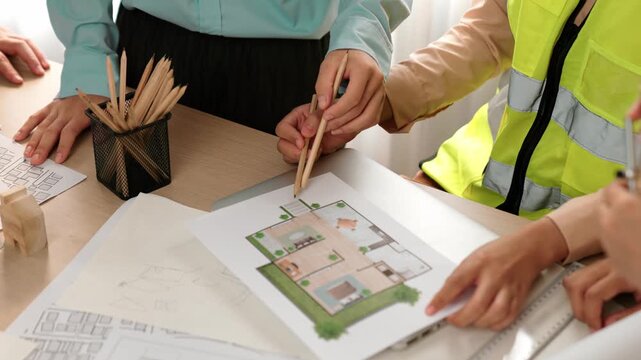 Smart architect and safety engineer discussion about building blueprint on table with architectural document, measurement tools and wooden block scatter around at modern office. Closeup. Delineation.