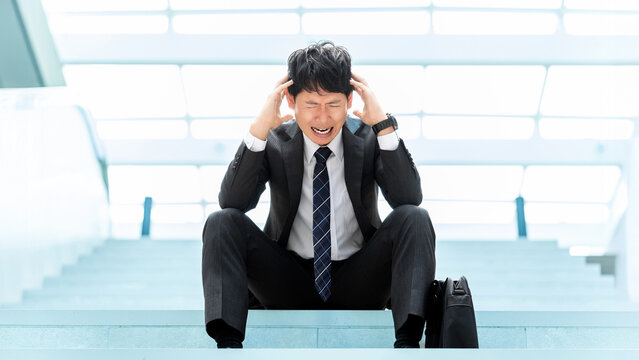 仕事のストレスで頭を抱えるビジネスマン, Stressed Businessman Holding His Head in Office Stairs Scene