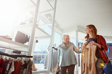 Obraz premium Shopping, senior mother and adult daughter in boutique, fashion advice and clothes guidance for bonding. Low angle, flare and happy people with apparel discount in retail store, space and helping