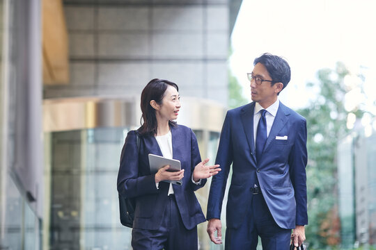 会話をしながら屋外を歩くビジネスマンとビジネスウーマン