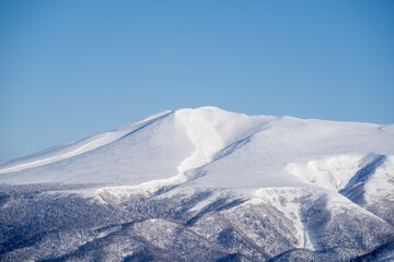 Mount Unabetsu in winter under a clear blue sky, vast snowy ridgelines and forests creating a powerful and tranquil landscape in Hokkaido