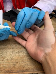 Medical professional wearing blue gloves inserting needle into patient. Person lying on medical chair with intravenous drip attached to their arm for blood transfusion or donation.
