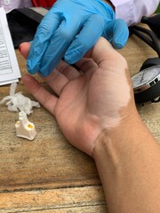 Medical professional wearing blue gloves inserting needle into patient. Person lying on medical chair with intravenous drip attached to their arm for blood transfusion or donation.