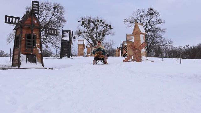 Beautiful girl sledding on a snowy slope among wooden buildings. Winter outdoor recreation, active day and atmospheric snowy landscape.