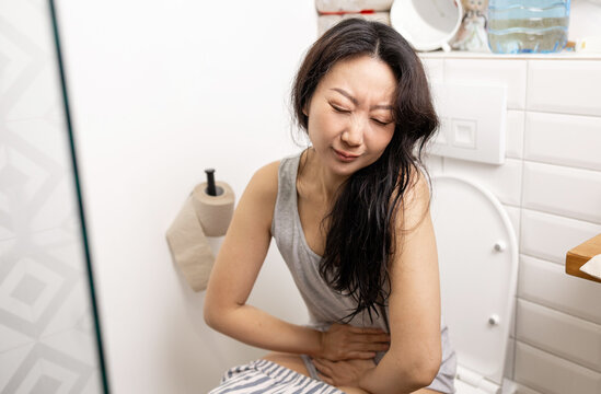 Asian woman sitting on toilet bowl. digestion, constipation, Diarrhea from food poisoning, infection, abdominal, stomachache, cystitis, Insurance, Health care and Medical