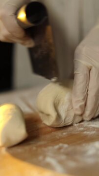 Woman cutting dough into portions in kitchen