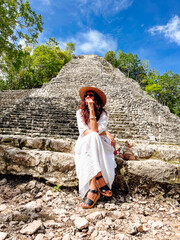 Fototapeta premium Visiting an ancient ruin in the forest during a sunny day. A person sits at the base of a stone structure surrounded by trees on a sunny day.