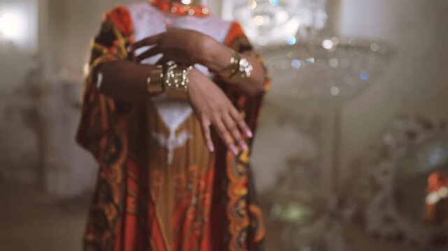 Black woman in ethnic african gown demonstrating golden jewelry on hands. Beautiful young lady dancing and showing her bracelets, traditional arabic dance show, closeup view of female arms and body