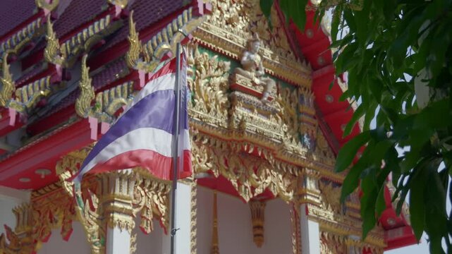 Close-up of the Thai national flag waving in the wind with the ornate golden Wat Nai Harn Buddhist temple in the background. High-quality 4K cinematic footage of Thai culture and architecture.