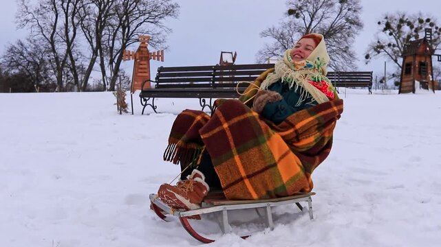 Beautiful girl sledding with a smile on her face. Joyful atmosphere, snow, active recreation, traditional clothing, beauty of nature and winter entertainment.